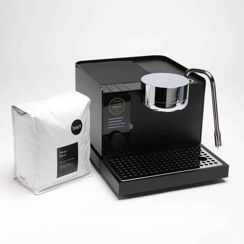 Black coffee machine with a silver spout and a white bag of coffee beans on a light gray background